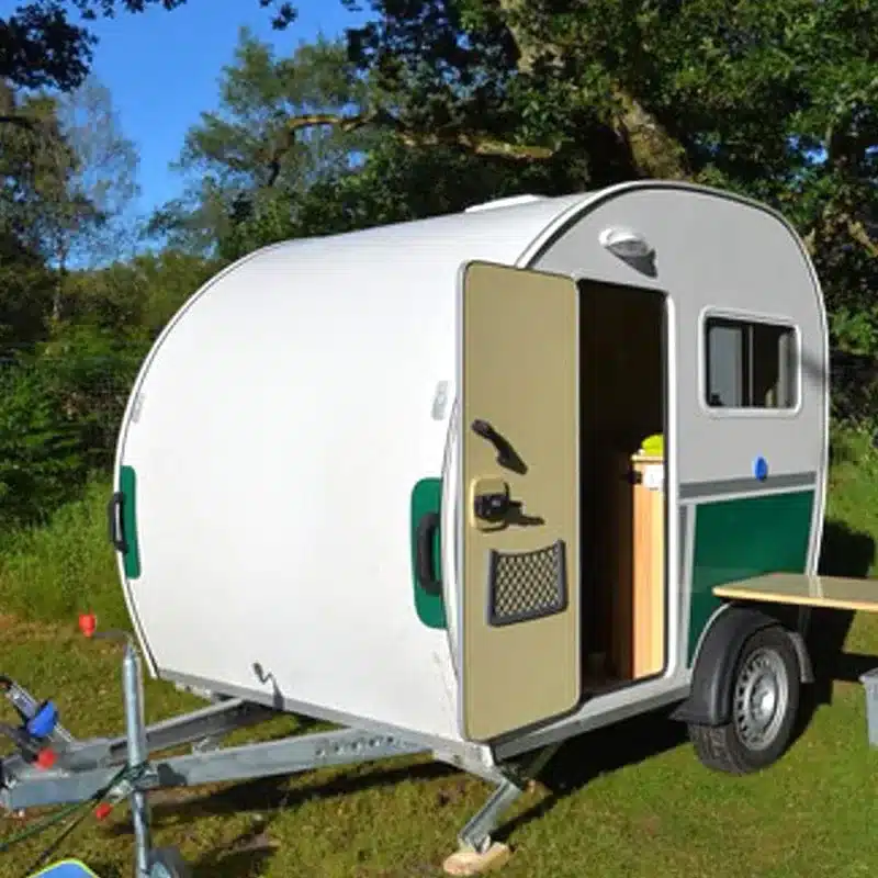 Der Kalala Teardrop Camper Trailer als ultrakompakter Wohnanhänger auf einer Wiese, Tür geöffnet.