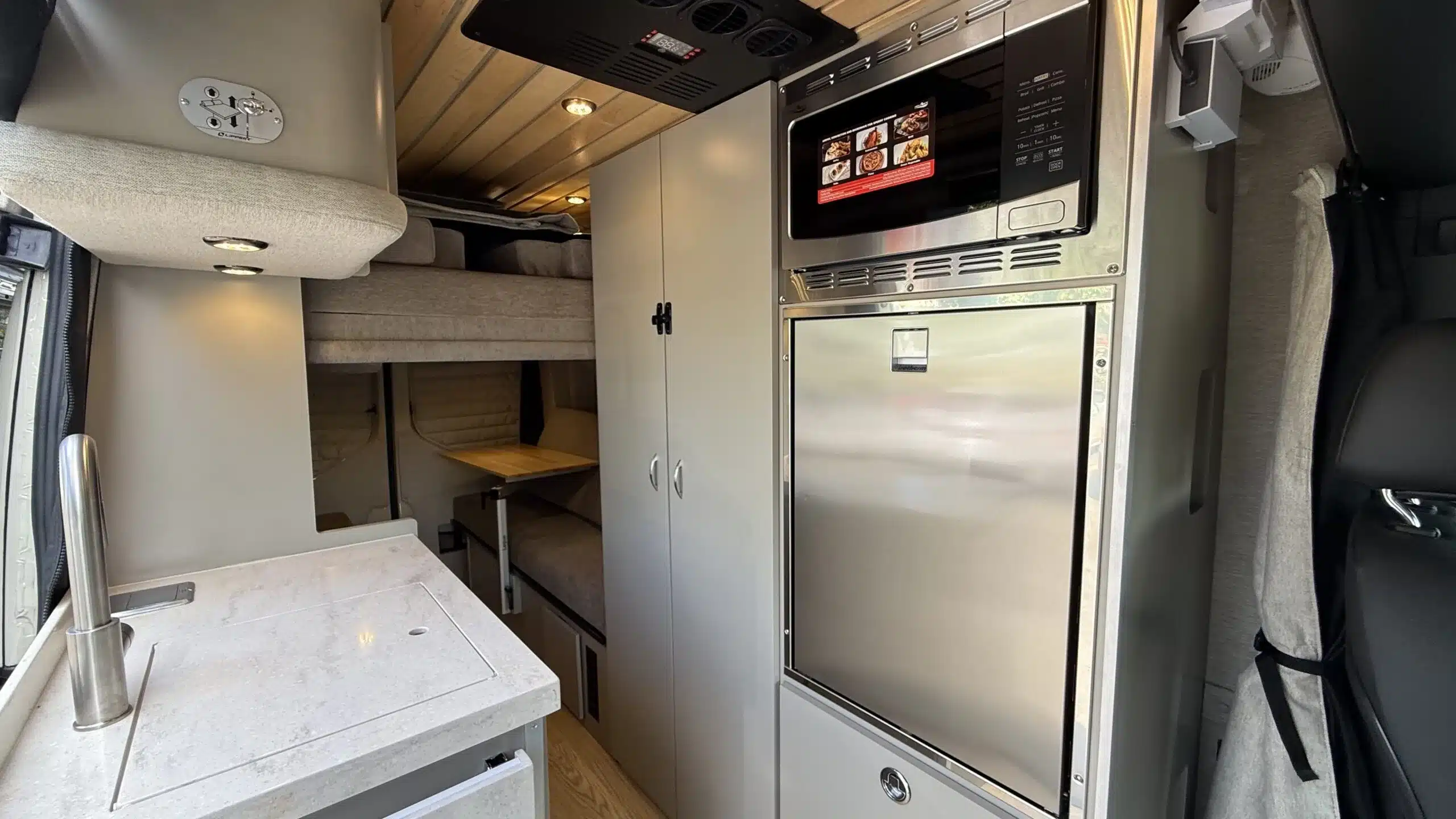 Moderne Campervan-Innenausstattung mit Küchenmodul, Stauraum und Schlafbereich für zwei Personen.