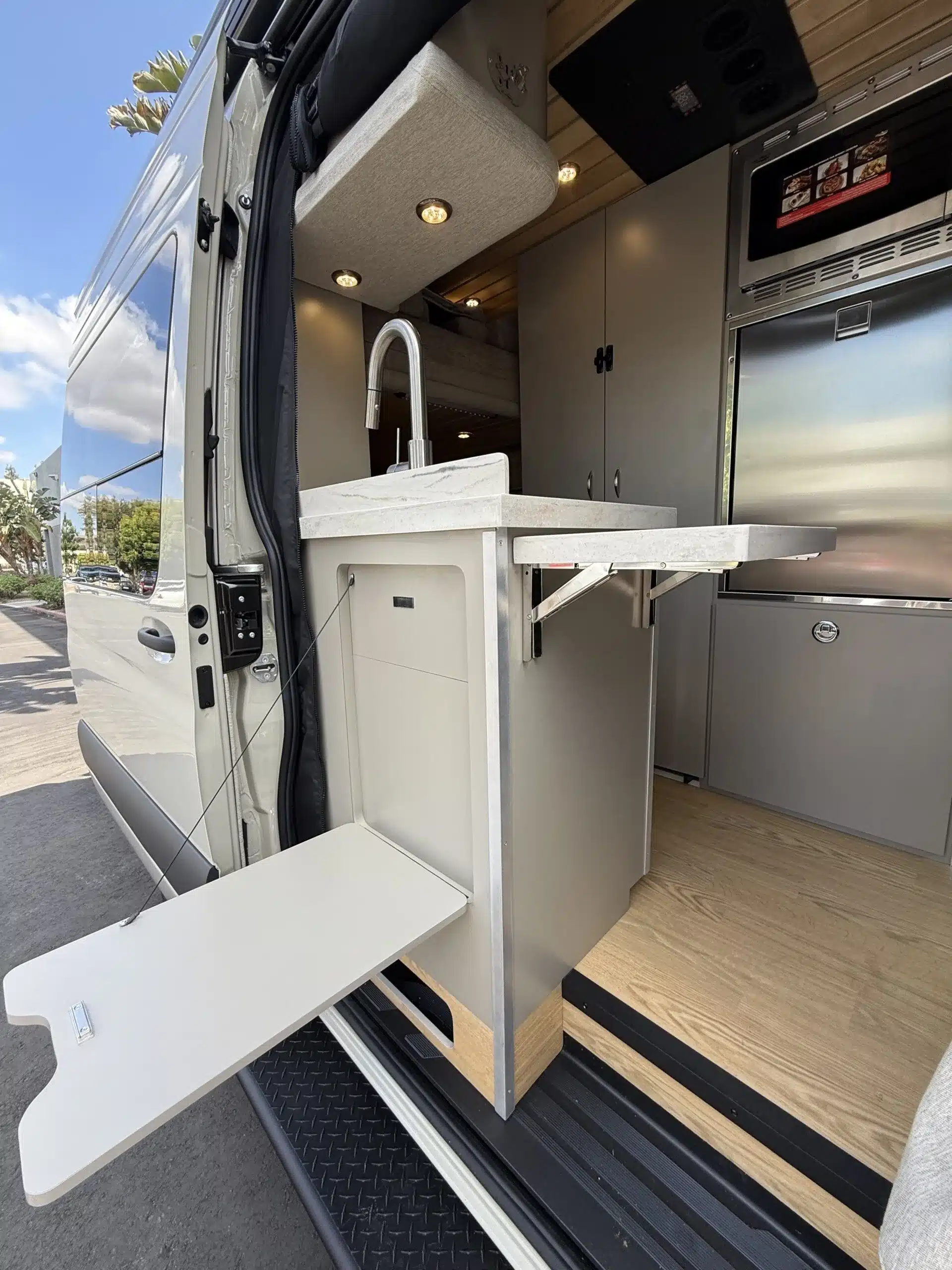 Innenansicht einer Campervan-Küche mit moderner Ausstattung und ausklappbarer Arbeitsplatte