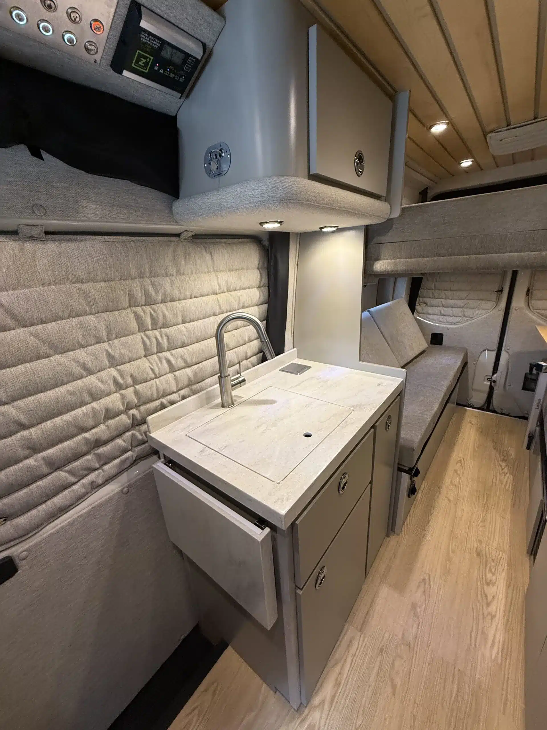 Moderner Innenraum eines kompakten Campervans mit Küchenzeile, Stauraum und Sitzbereich, ausgelegt für zwei Personen.