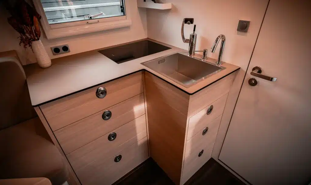 L-förmige Küche mit Induktionskochfeld, Edelstahlspüle und Schubladen im Expeditionsfahrzeug Krug Project Rhino 4300.