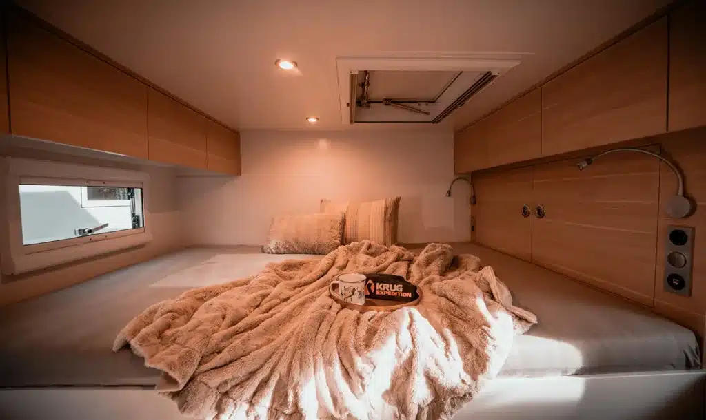 Doppelbett mit Tagesdecke und Kissen im Innenraum eines Krug Project Rhino 4300 Expeditionscampers