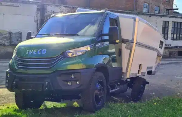 Grünes Expeditionsmobil Laske LE410 mit Wohnkabine und Offroad-Fahrwerk, seitlich vorgestellt vor alten Industriegebäuden.