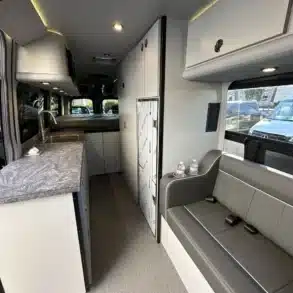 Blick in den großzügigen und modernen Innenraum eines ausgebauten Mercedes Sprinter Campervans, mit Küche, Sitzbank und Stauraum.