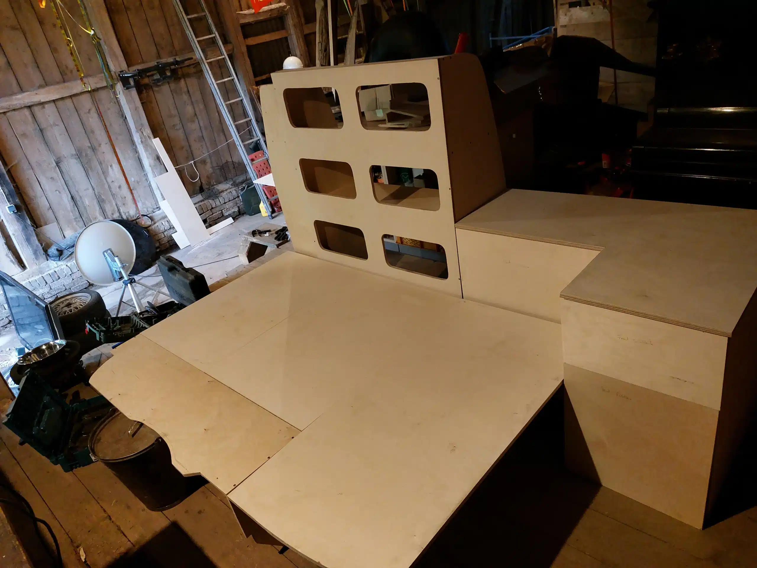 Unbehandelter Möbelbausatz aus Multiplexholz mit Bett- und Schrankmodulen in einer Werkstattumgebung, vorbereitet für den Einbau in einen Ford Transit Custom.