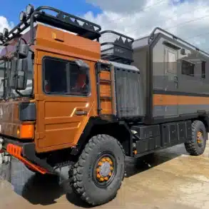 Seitenansicht des MAN HX60 Overland Expeditionsfahrzeugs mit orangefarbener Fahrerkabine und grauem Wohnaufbau, ausgestattet für Fernreisen und Offroad-Einsätze.