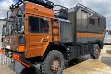 Seitenansicht des MAN HX60 Overland Expeditionsfahrzeugs mit orangefarbener Fahrerkabine und grauem Wohnaufbau, ausgestattet für Fernreisen und Offroad-Einsätze.