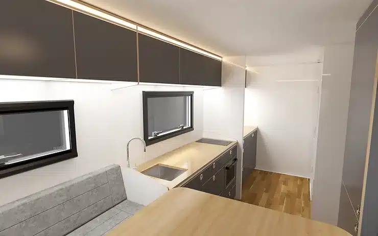 Innenansicht der Küche und des Essbereichs eines modernen Expeditions-Lkw mit hellen Holzarbeitsflächen, grauen Schränken und Sitzbank.