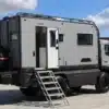 Seitenansicht eines ausgebauten Mercedes Atego 4x4 Expeditionsmobils mit Wohnkoffer, Dachträger und geöffneter Tür mit Treppe.