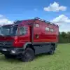 Rotes Mercedes-Benz Axor 1829 Expeditionsmobil auf einer Wiese, Allradfahrgestell und große Wohnkabine mit mehreren Fenstern.