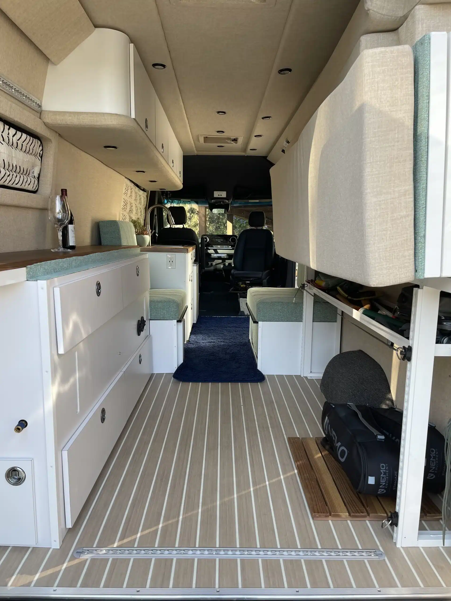 Innenansicht eines Mercedes Sprinter 170 Adventure-Van mit weißem Ausbau, grünen Akzenten, Küche und Sitzgelegenheiten.