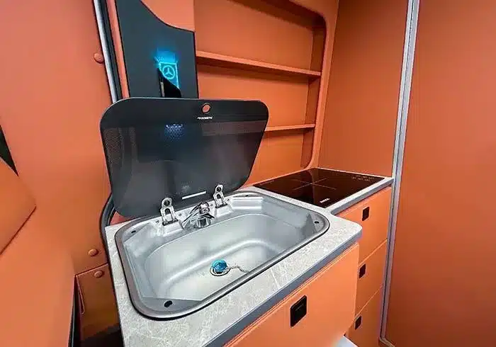 Küche mit Edelstahl-Spüle, Induktionskochfeld und Stauraum im Mercedes Sprinter T1‑C Camper