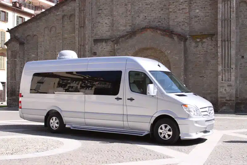Silberner Mercedes-Benz Sprinter Umbau als luxuriöser VIP Van Conversion von Delta Automotive auf einem Platz vor einer historischen Steinmauer