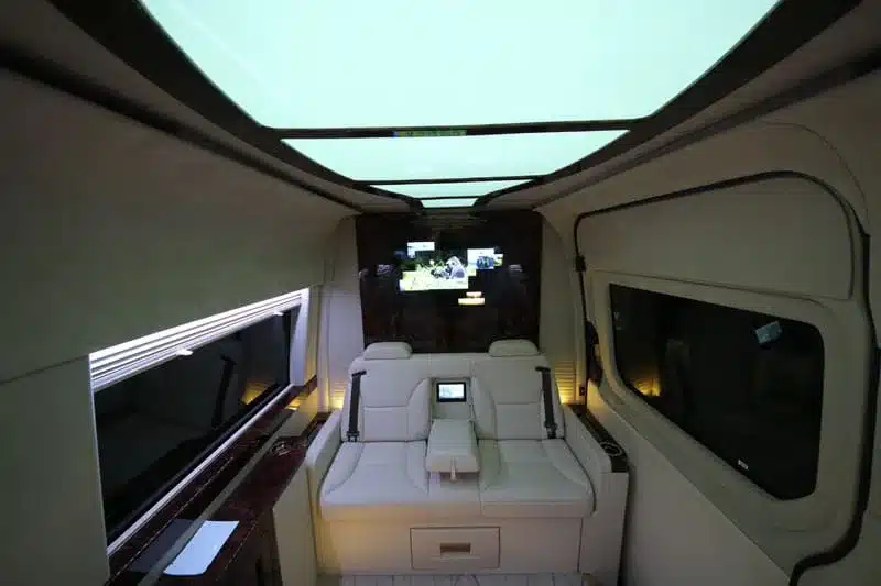 Innenansicht eines luxuriös ausgebauten Mercedes Sprinter Vans mit LED-Beleuchtung, großen Sitzen und Technik-Panel.