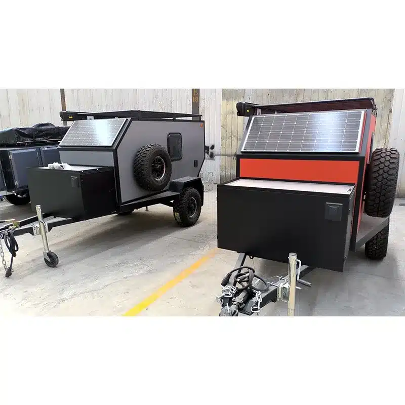 Zwei Mini 2B Offroad-Camper Trailer mit Ersatzrad und Solarpanel, abgestellt in einer Halle.