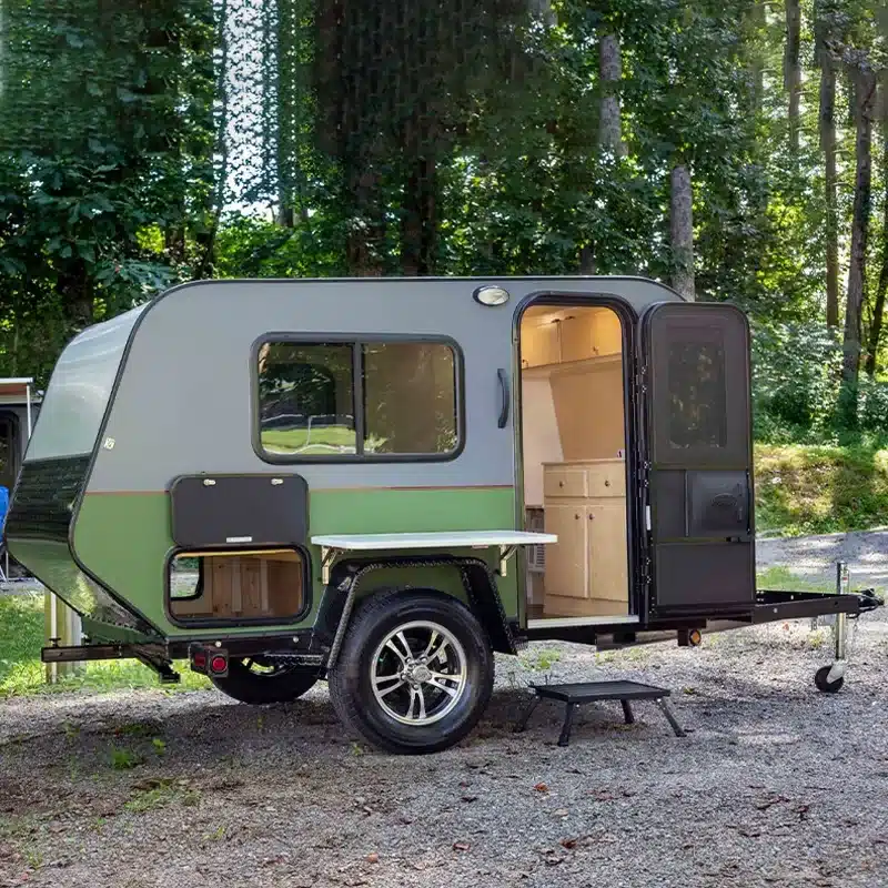 Mini 2D Offroad-Camper-Trailer mit geöffneter Tür auf Waldboden, Seitenansicht mit Fenster und Küchenmodul sichtbar