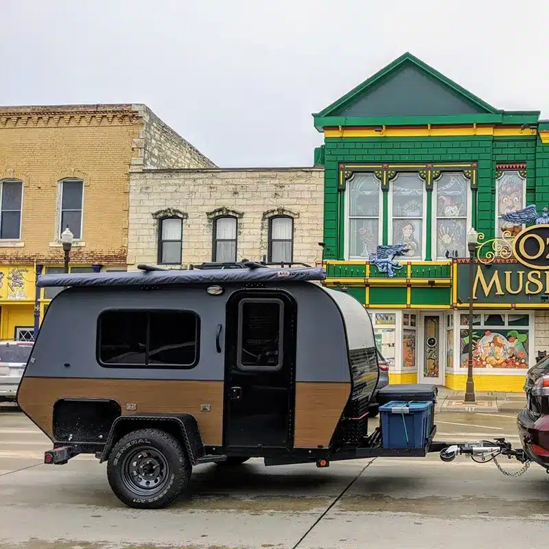 Seitenansicht eines Mini 2D Offroad-Camper-Trailers, der von einem Auto durch eine Stadt gezogen wird.