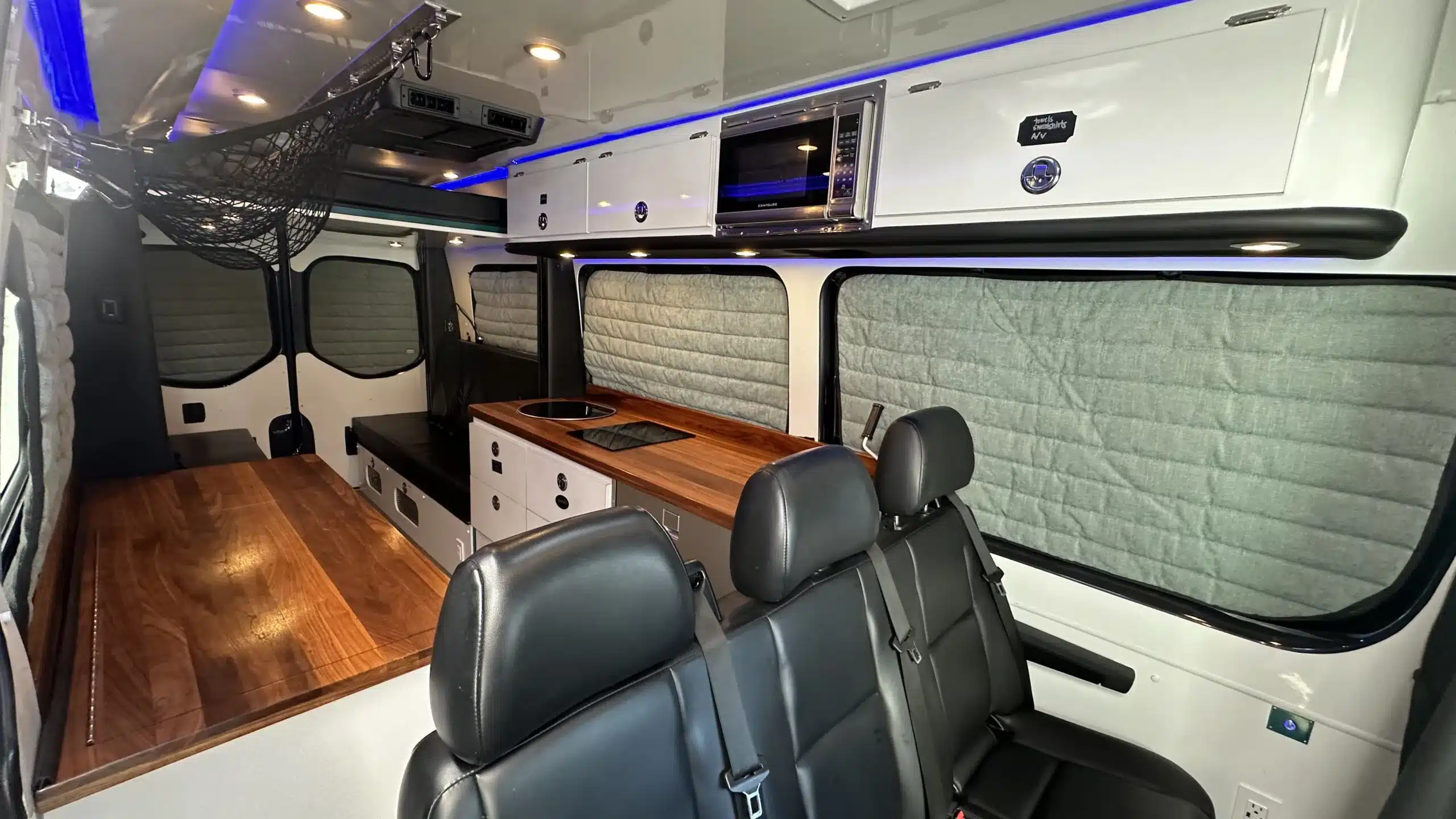 Innenansicht eines ausgebauten Sprinter-Campervans mit Sitzbank, Küchenzeile und Staufächern.
