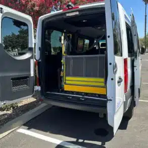 Offene Hecktüren eines Vans mit eingebautem gelbem Rollstuhllift in einer Parkumgebung.