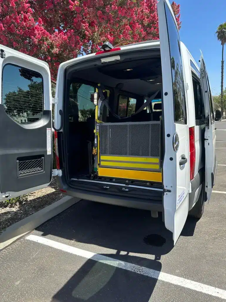Offene Hecktüren eines Vans mit eingebautem gelbem Rollstuhllift in einer Parkumgebung.