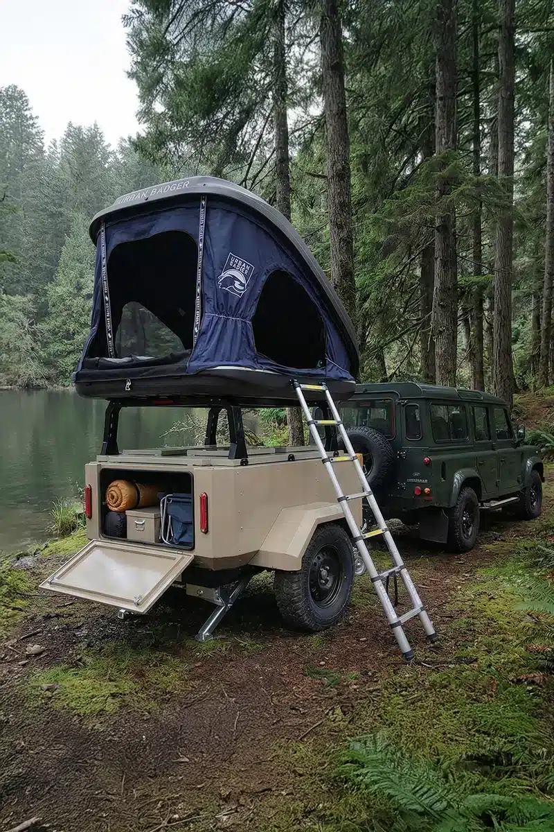 Campingtrailer mit Dachzelt und Geländewagen am Waldrand neben einem See