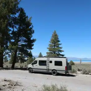 Motherload Campervan, geparkt in der Naturlandschaft mit Bergsee und Kiefern im Hintergrund.