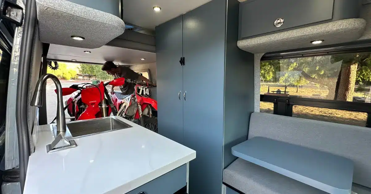 Blick in den ausgebauten Mercedes Sprinter 170 mit Küchenzeile, Sitzbank und verladenen Motocross-Motorrädern.