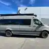 Seitenansicht des ausgebauten Mercedes Sprinter 170 4x4 Campervans Nala, geparkt vor einem Gebäude bei Sonnenschein.