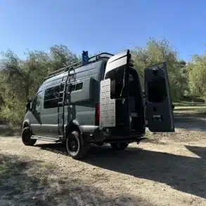 Mercedes Sprinter 144 AWD Campervan Nestor mit Dachträger und geöffneter Hecktür auf Waldweg