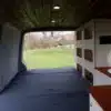 Kompakter VW T5 Innenausbau mit ausgeklapptem Bett, Küchenmodul und Stauraumschrank im Campingbus.