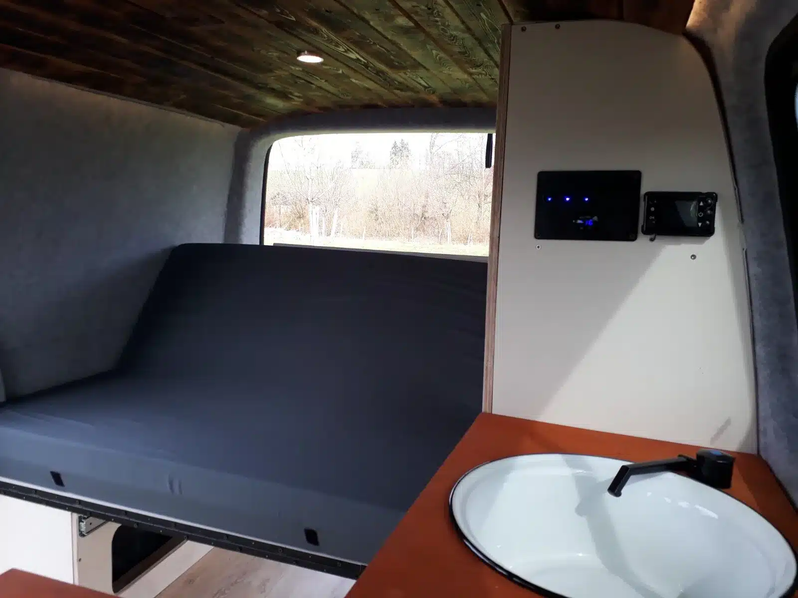 Innenansicht eines VW T5 mit Klappbett, hohem Schrank und eingebautem Spülbecken