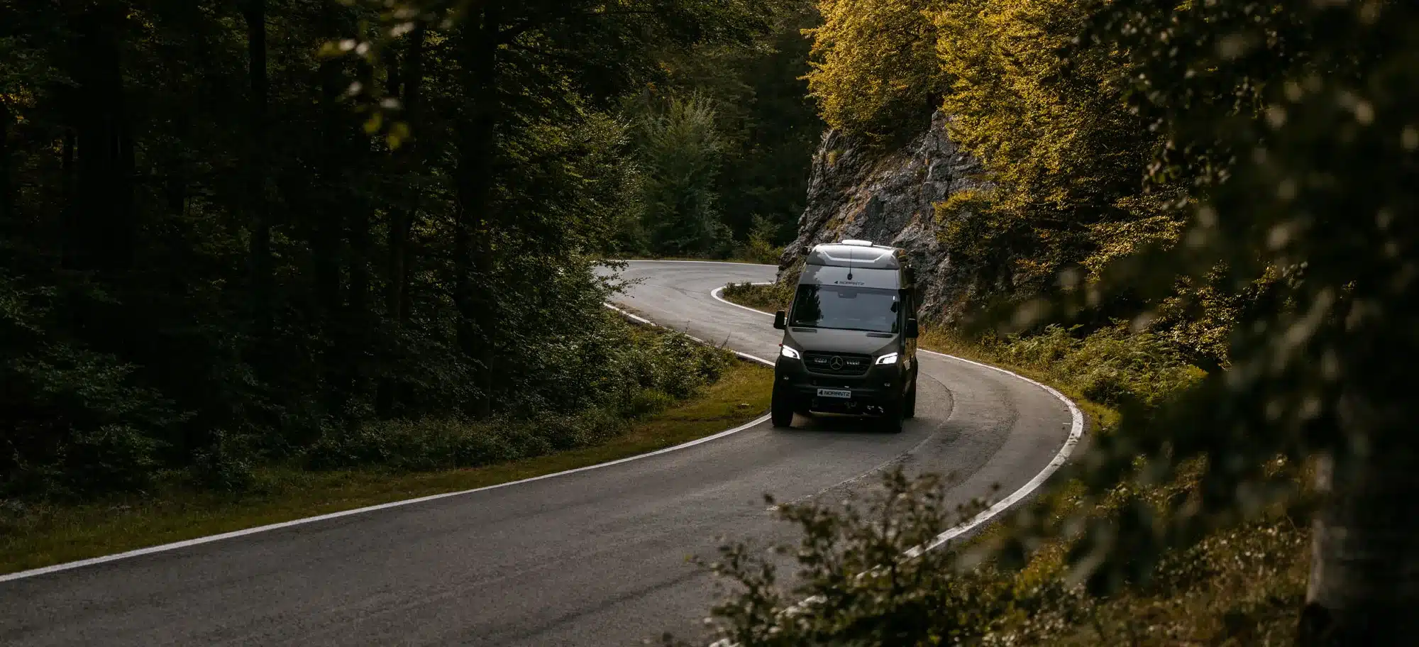 Ein NORANTZ EKI Camper Van auf einer kurvigen Straße im Wald, von vorne aufgenommen.