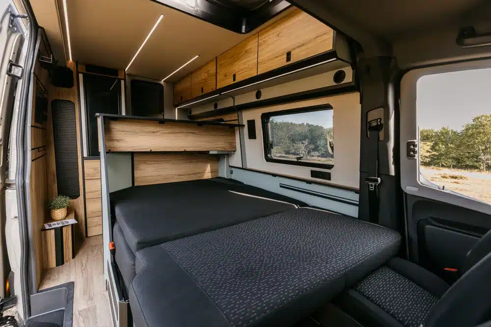 Innenansicht eines NORANTZ EKI Camper Vans mit flexiblem Bett und modernen Holzoberflächen.