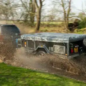 Off-Road Air OPUS Faltcaravan an einem Zugfahrzeug, fährt durch eine nasse Schlammpfütze im Gelände