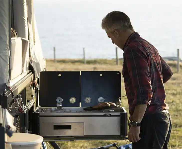 Externe Outdoor-Küche eines Offroad-Faltcaravans mit Camper am Kocher, Ufer und Meer im Hintergrund