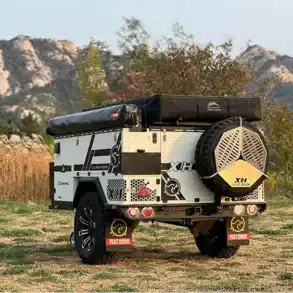 Patriot X1H Travel Trailer auf einer Wiese vor Felsen, Offroad-Anhänger für Camping und Abenteuerreisen.