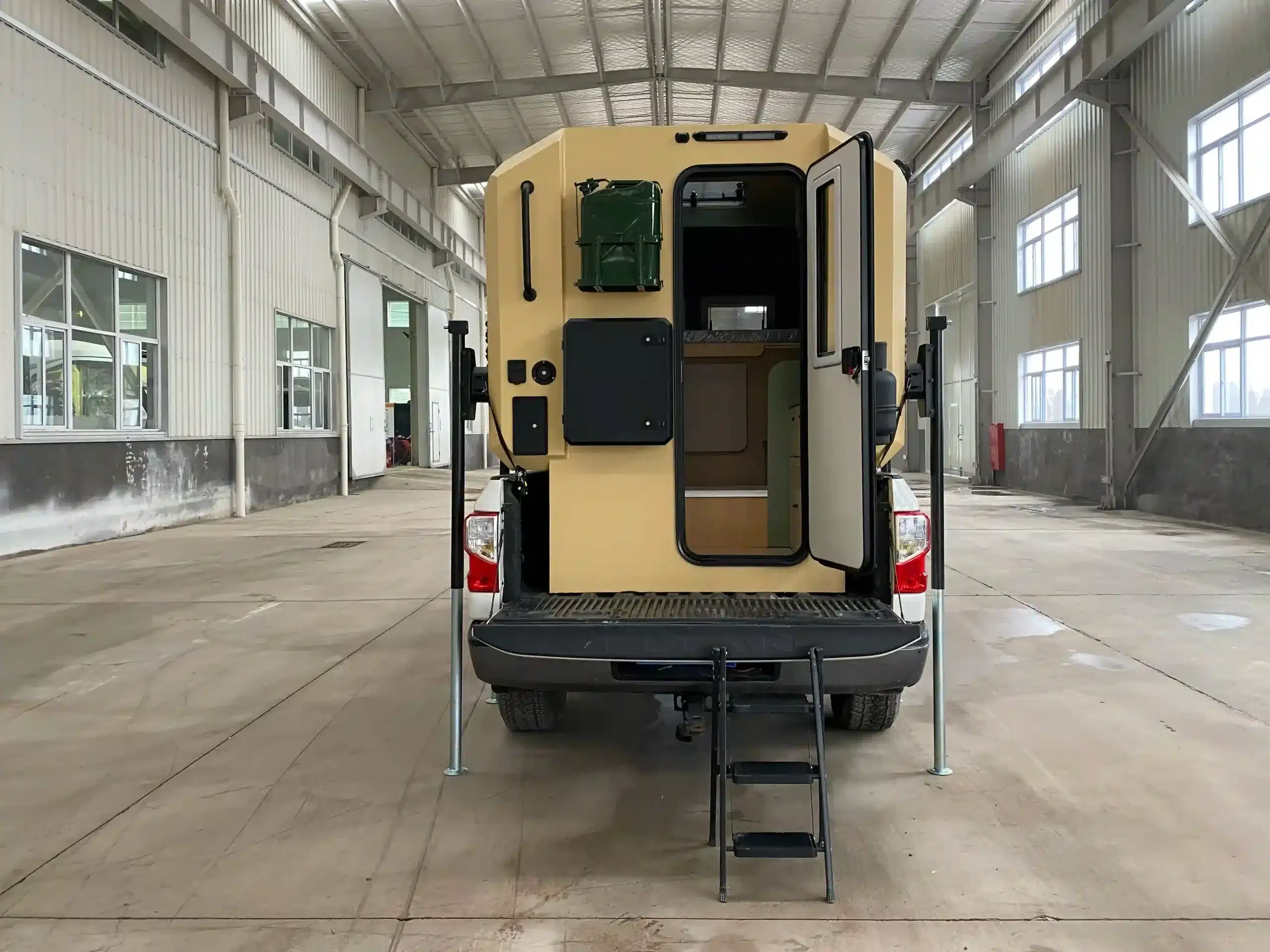 Pickup mit montierter Wohnkabine, geöffneter Tür und Einstiegstreppe in einer Halle, Sicht von hinten.