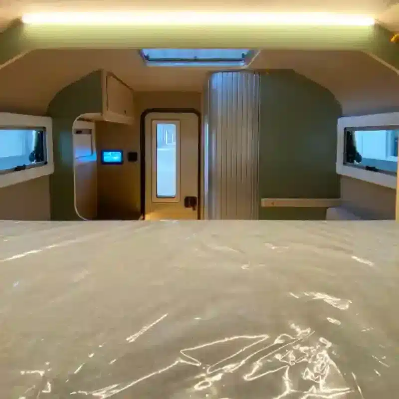 Innenraum eines leichten Pickup Truck Campers mit Sicht auf Bad, Tür und Fenster vom Bett aus