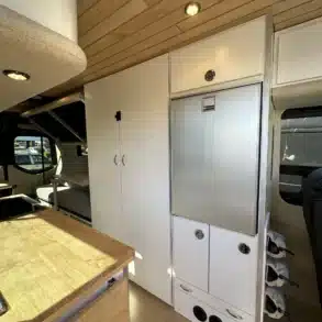 Innenraum eines Raven Adventure Vans mit Küche, Arbeitsfläche, großem Kühlschrank, Schränken und integriertem Weinflaschenhalter
