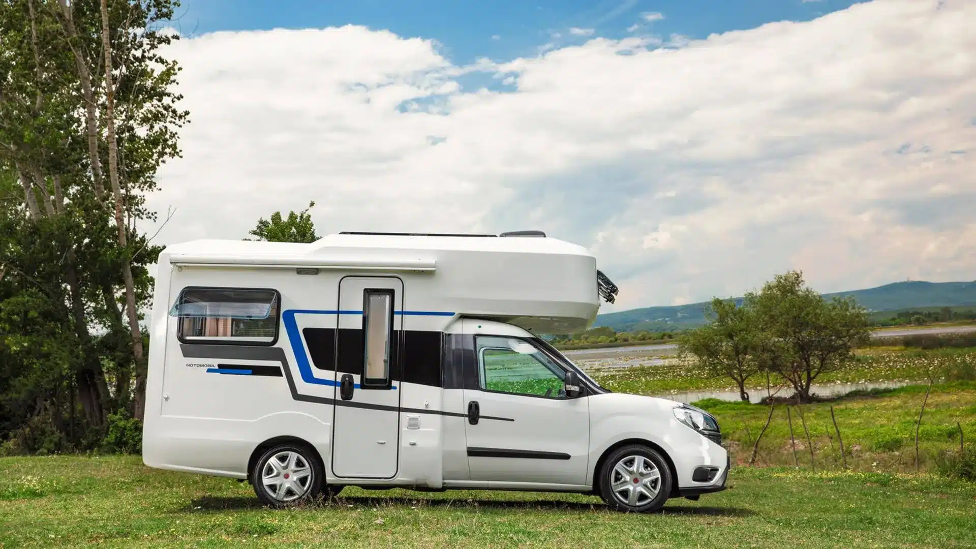 Seitenansicht eines weißen Ronin XL Motorhome Campers auf einer Wiese vor bewölktem Himmel.