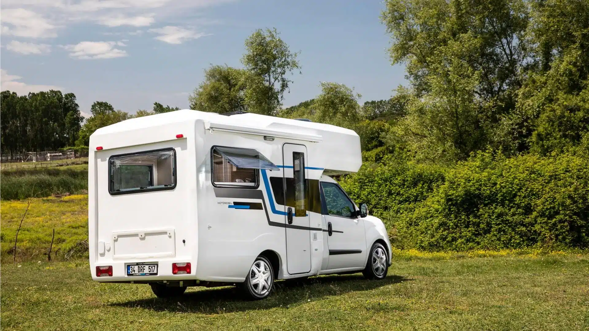 Seitenansicht des Ronin XL Motorhome mit geöffneter Fensterklappe, parkend auf einer Wiese vor Bäumen.