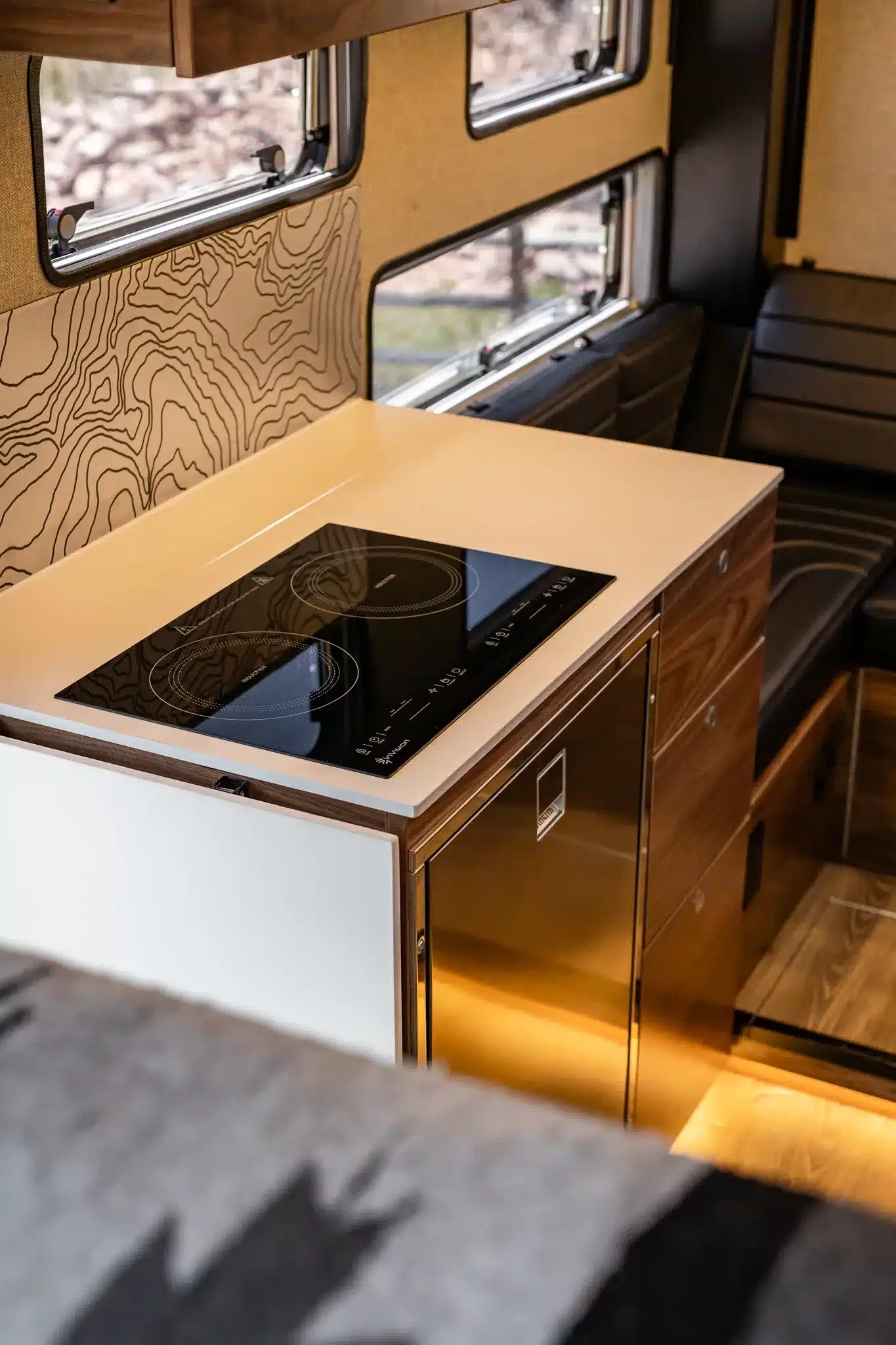 Moderne Camperküche mit Induktionskochfeld, Holzoberflächen und Stauraum im Rossmönster Baja Truckcamper