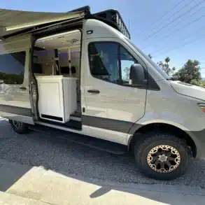 Mercedes Sprinter 144 AWD Campervan Serenity mit offenem Einstieg und Markise, zeigt Küchenblock und modernen Innenraum.