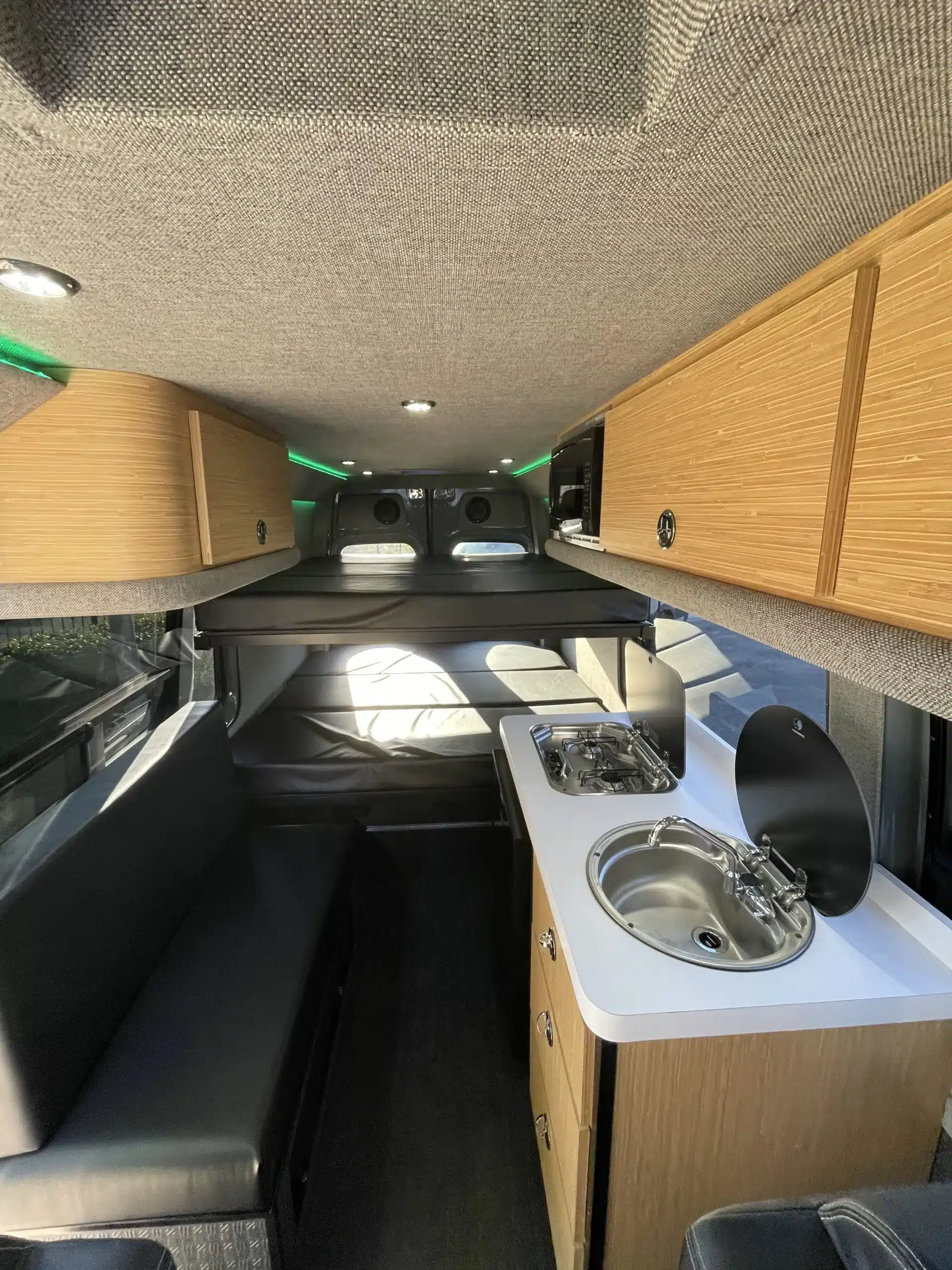 Innenansicht eines Sprinter 170 4x4 Campervans mit Küchenzeile, Sitzbank und Bett im Fond.