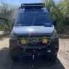 Frontansicht eines ausgebauten Mercedes Sprinter 4x4-Campers mit Zusatzscheinwerfern, Dachträger und Seilwinde im Gelände.