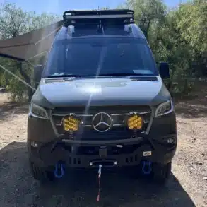 Frontansicht eines ausgebauten Mercedes Sprinter 4x4-Campers mit Zusatzscheinwerfern, Dachträger und Seilwinde im Gelände.
