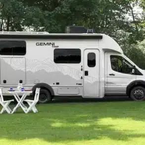 Gemini AWD Reisemobil von Thor Motor Coach, seitlich geparkt auf einer Wiese, mit Campingmöbeln davor.