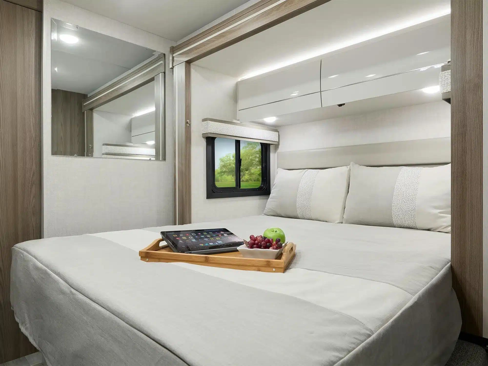 Kingsize-Bett im Heckbereich des Thor Gemini AWD 24KB mit Tablett, Tablet und Obst, ergänzt durch moderne Schränke und Fenster.
