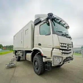 Frontansicht eines TITAN 60 UQX 4x4 Expeditionsmobils auf Mercedes Arocs Basis mit Einstiegstreppe im Freien.