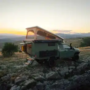 Toyota Hilux Trailcat Expeditionsfahrzeug mit geöffneter Wohnkabine und Aufstelldach in naturbelassener Umgebung bei Sonnenuntergang